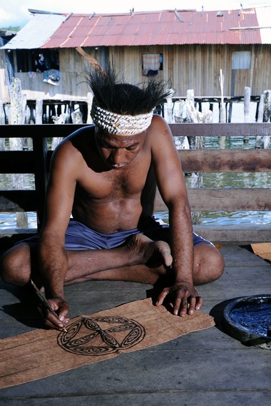 Pelukis kulit kayu sedang menggoreskan tinta pada lembaran kulit kayu