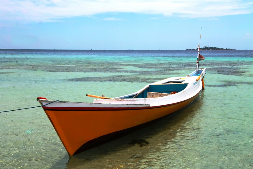 Sebuah perahu bersandar di pulau Barang Caddi dengan latar belakang Pulau Barang Lompo